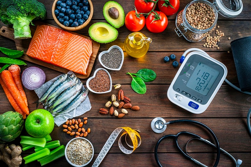 Colorful foods surrounding a blood pressure meter, stethoscope and measuring tape.