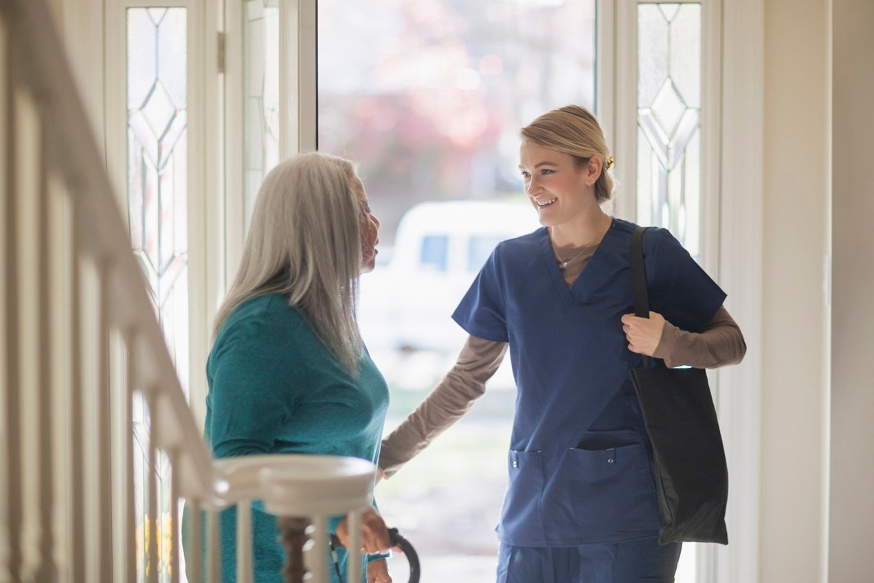A home health care worker greets her patient in their doorway